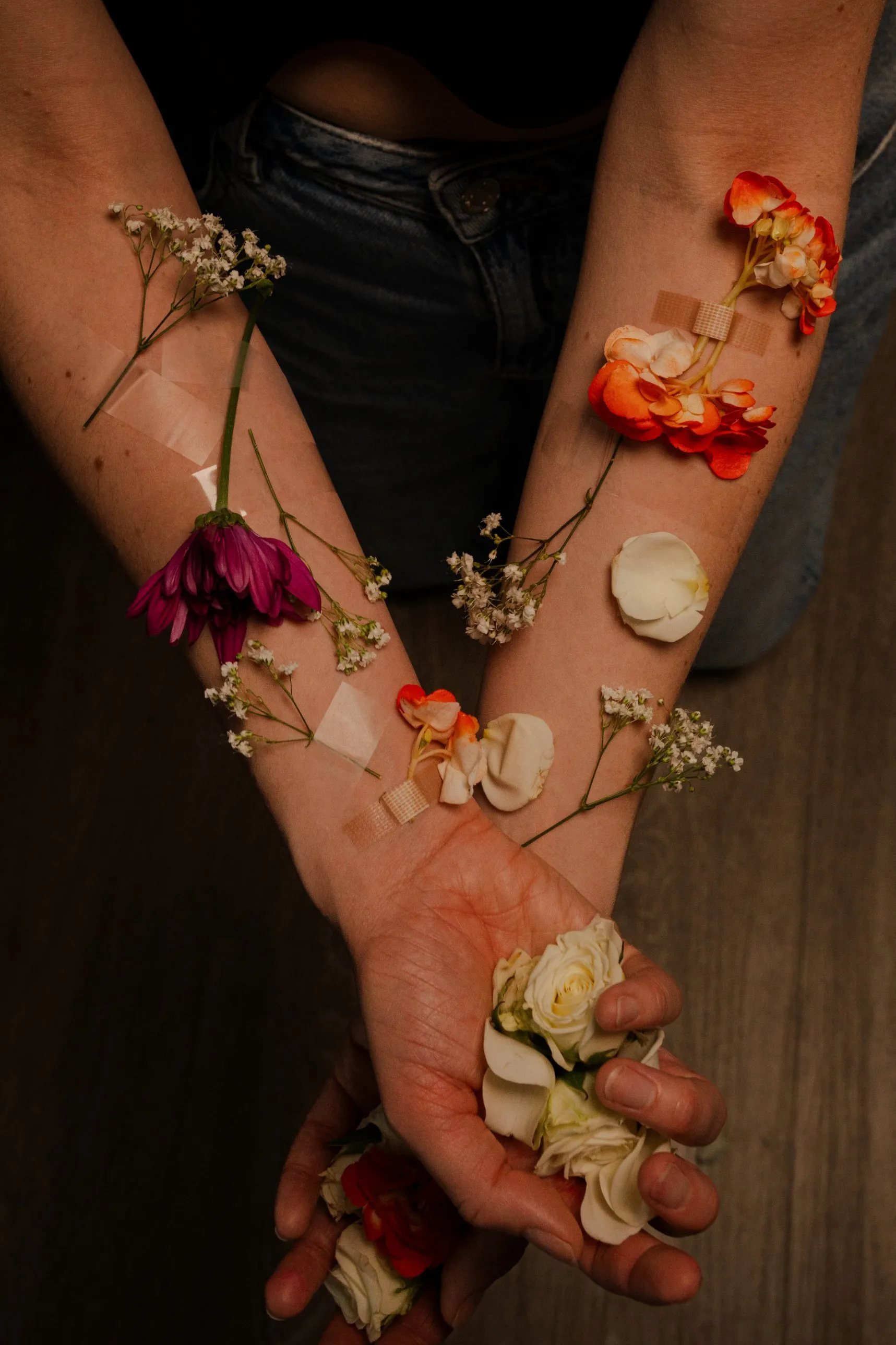 Deux avant-bras croisés, couverts de fleurs fixées à la peau avec du ruban adhésif, une main pleine de roses